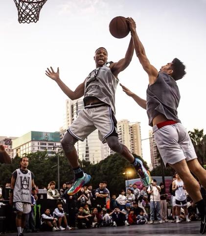 Two athletes battling for a rebound in front of a courtside crowd